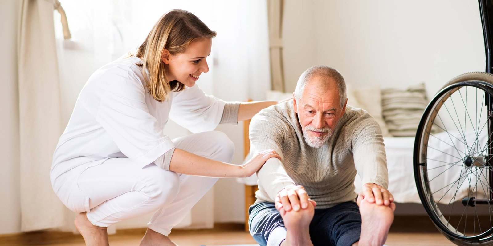 Health visitor and a senior man during home visit. A nurse or a physiotherapist helping a senior man exercise.